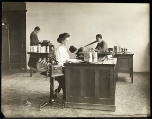 Interiörvy av en kvinna som skriver från en dikteringsmaskin och en man som dikterar i en annan på Edison Phonograph Co., West Orange, New Jersey, 1903 (silvergelatintryck)